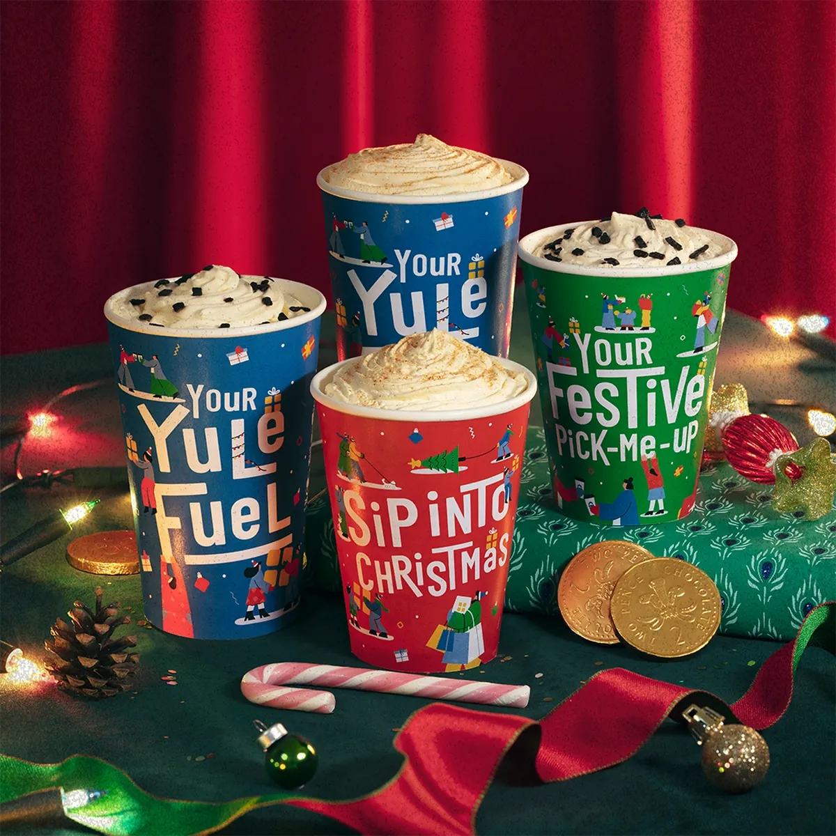 Four Greggs Christmas drinks topped with cream, in blue, red and green cups lettered Your Yule Fuel, Sip into Christmas and Your Festive Pick-me-up